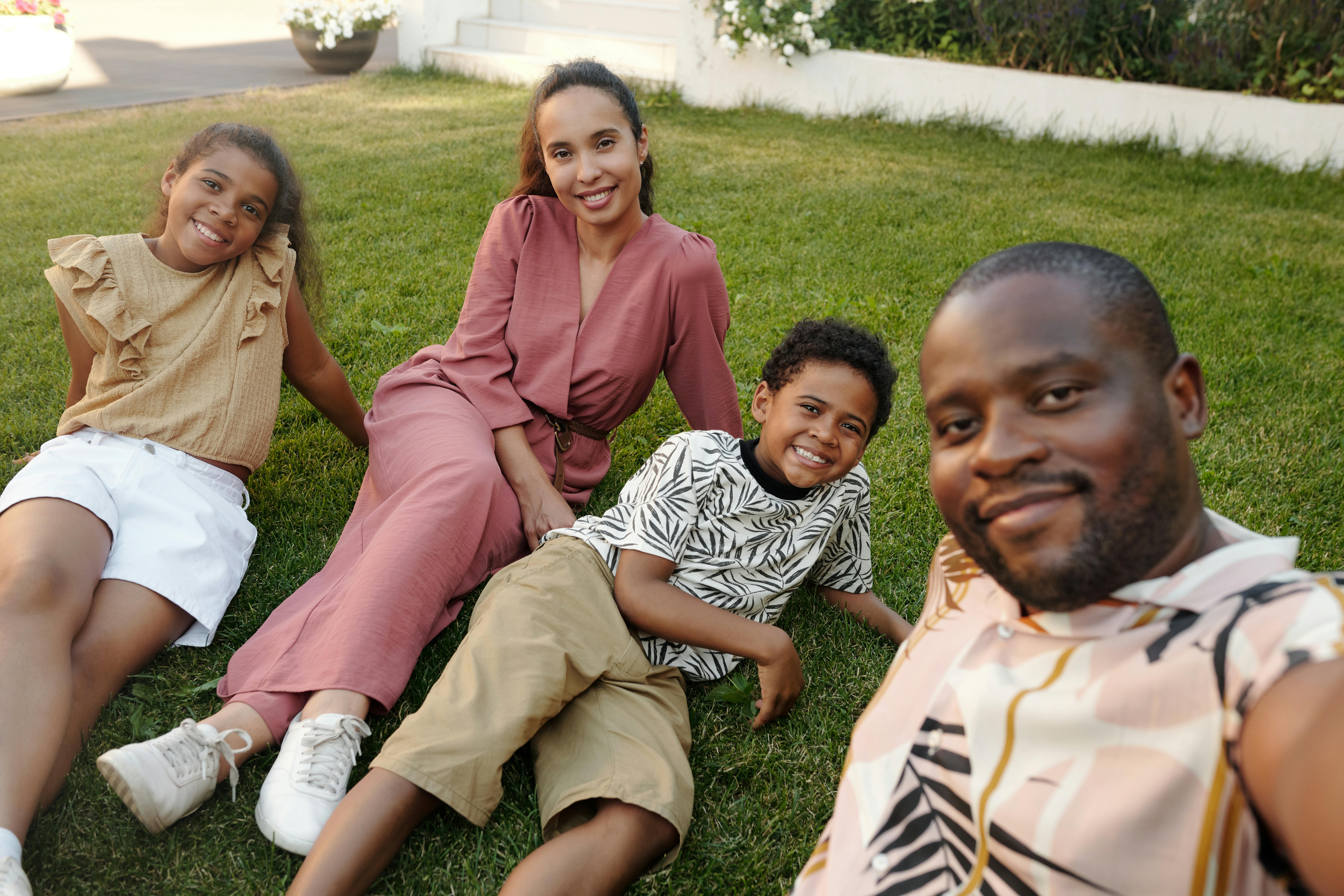 Smiling family relaxing together on the grass during summer break, enjoying a calm and connected moment outdoors.